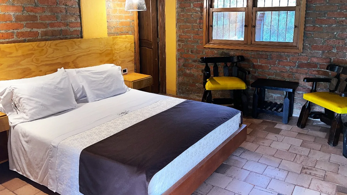 Habitación Doble: cama queen con ropa blanca, pared de ladrillo a la vista y suelo de barro cocido