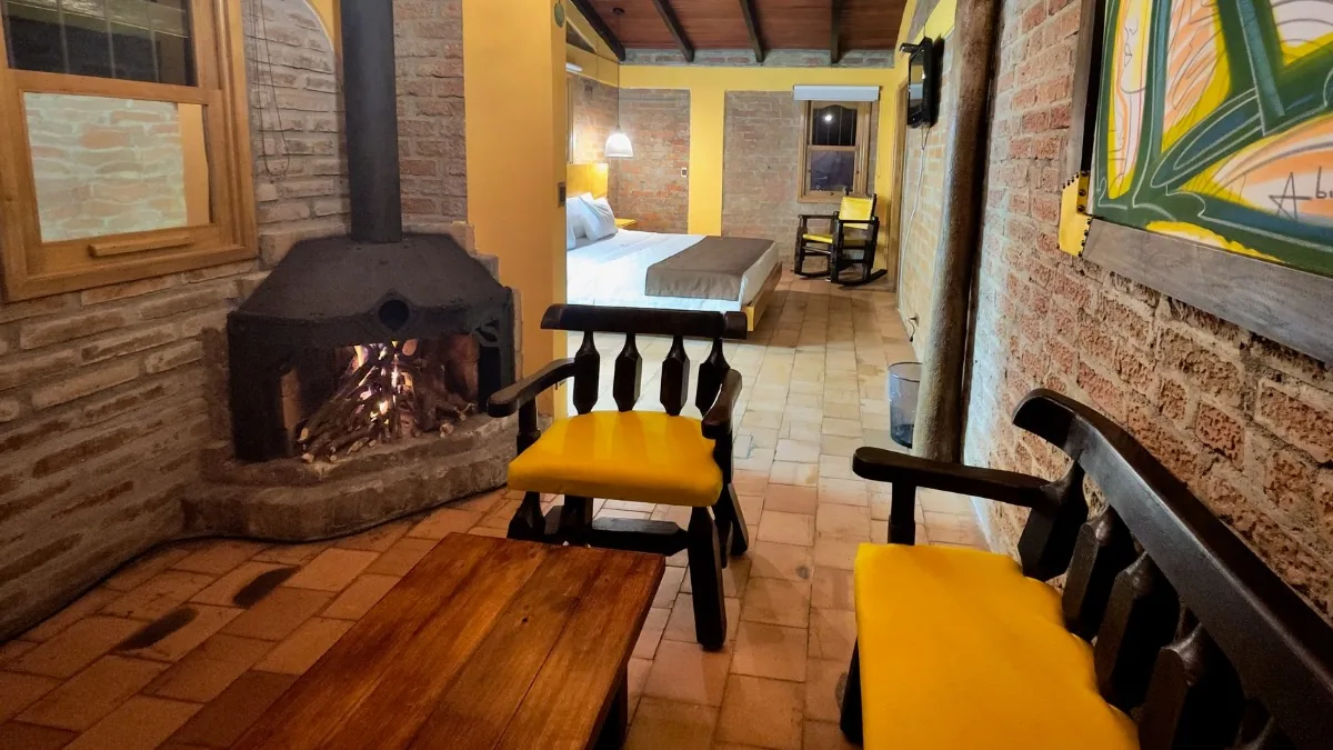 Suite Junior: chimenea de ladrillo encendida, mesa baja de madera y la cama al fondo